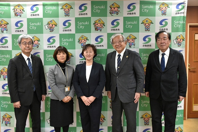 市長や副市長、教育長などとさぬき市のバックパネルの前で記念写真を撮る得丸委員