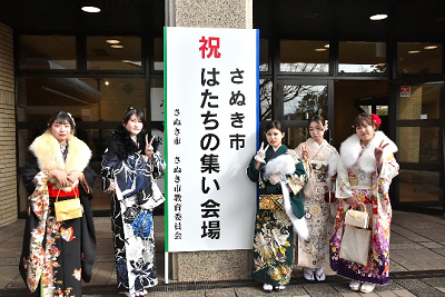 はたちの集いの立て看板の左右でピースする5名の振り袖姿の女性